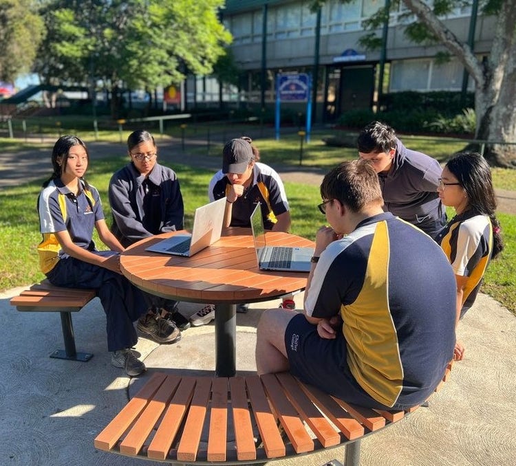 Students working on computers at table outdoors